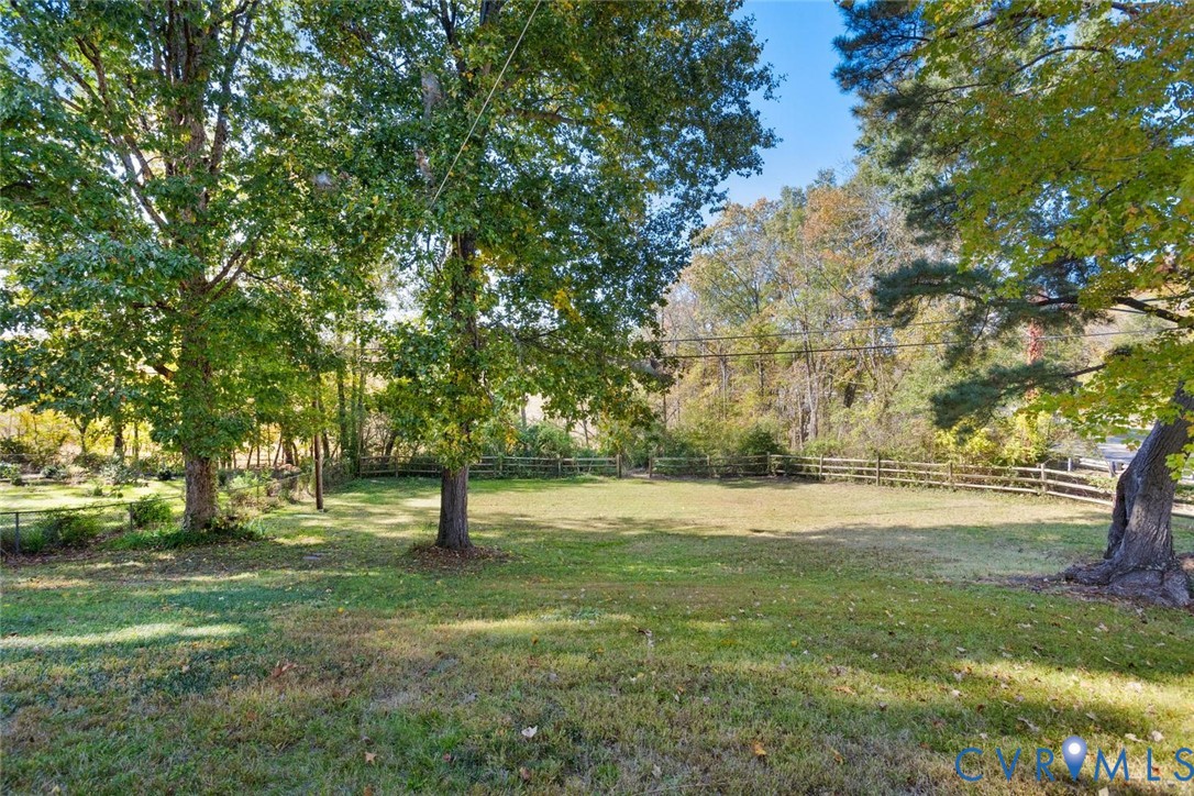Expansive backyard featuring mature trees, manicured lawn, and post-and-rail wood fencing