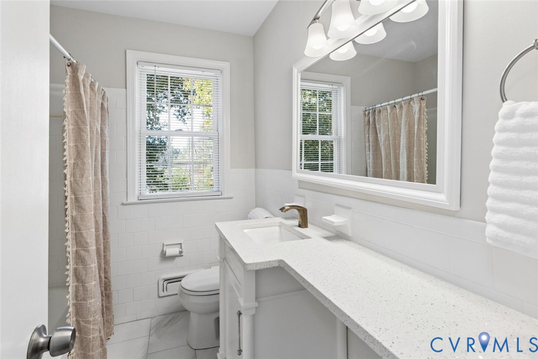Bathroom featuring a vanity with a white composite countertop, an integrated rectangular sink, a metallic faucet, a large framed mirror, and white subway-style wall tiling