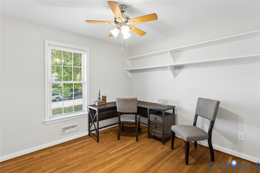 Room with wood-finish flooring, white wall-mounted shelving, a multi-pane window, and a ceiling fan with integrated lighting