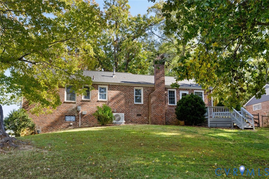 Brick exterior featuring an elevated wood deck, exterior chimney, and mature trees situated on a sloped lot