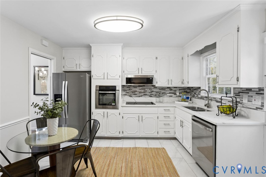 Kitchen featuring white cabinetry, stainless steel appliances, a multi-tone tile backsplash, quartz countertops, and tile flooring