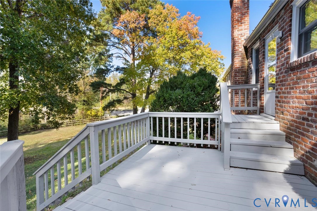 Elevated deck featuring painted wood-finish railing and stairs, exterior brick masonry, and a chimney stack