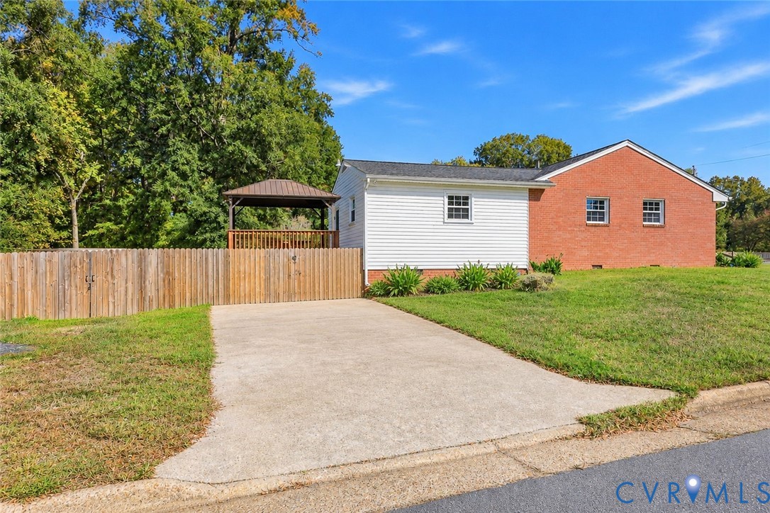 Exterior facade featuring red brick and white siding, concrete driveway, vertical wood privacy fencing, and a detached wooden gazebo