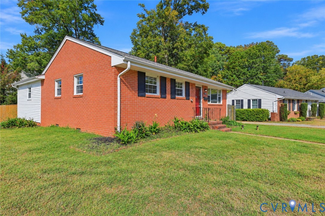 Red brick exterior featuring white siding accents, black window shutters, a front entrance with iron railing, and a sprawling lawn