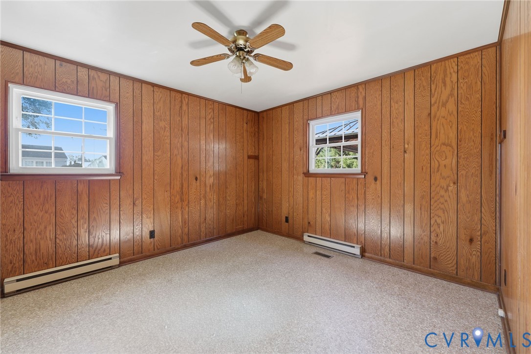 Interior space featuring wood-panelled walls, wall-to-wall carpeting, two double-hung windows, and a ceiling-mounted fan with light fixture