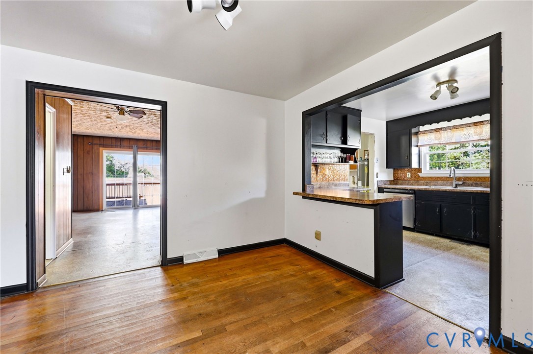 Hardwood flooring, kitchen pass-through window with a laminate countertop, black cabinetry, stainless steel dishwasher, and recessed ceiling lighting