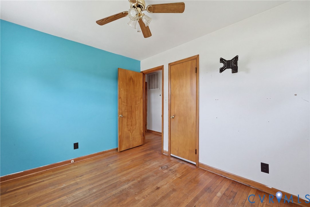 Room featuring wood-finish flooring, a ceiling fan with integrated lighting, and solid-core wood-finish doors