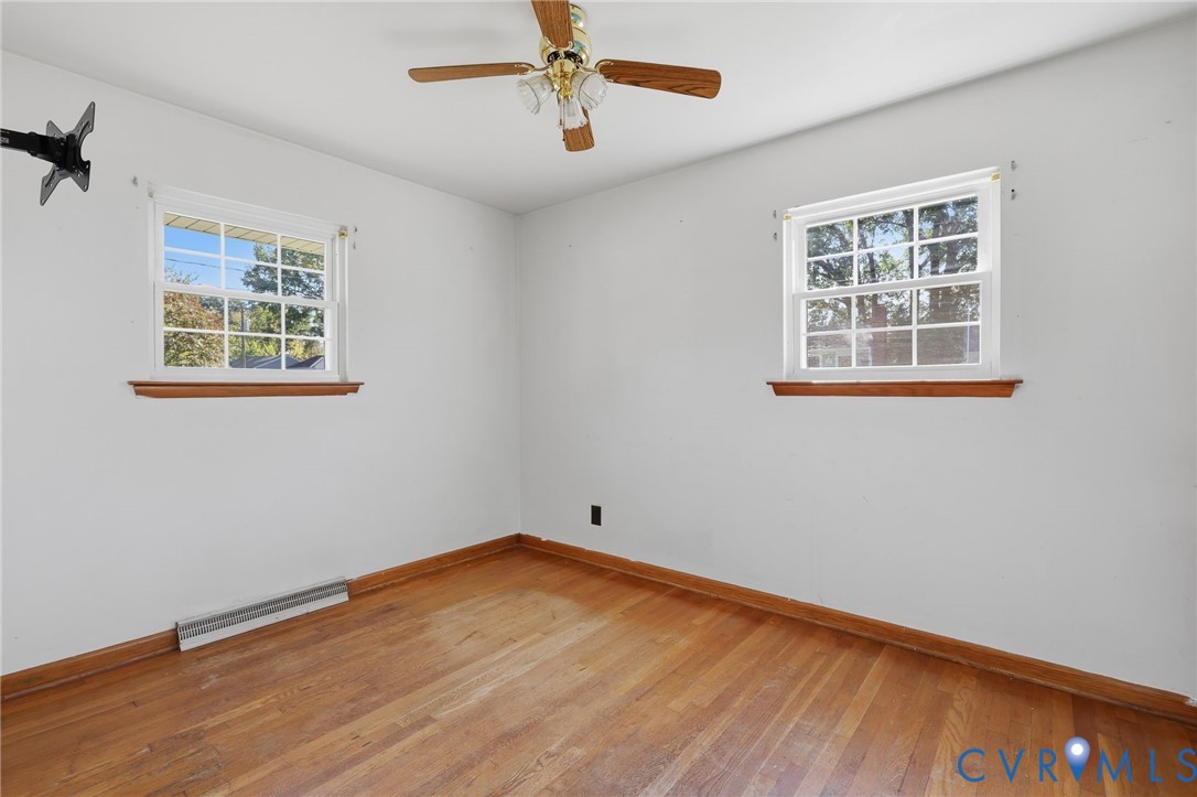Room featuring wood-finish flooring, two multi-pane windows with wood trim, and a ceiling-mounted light fixture with a fan