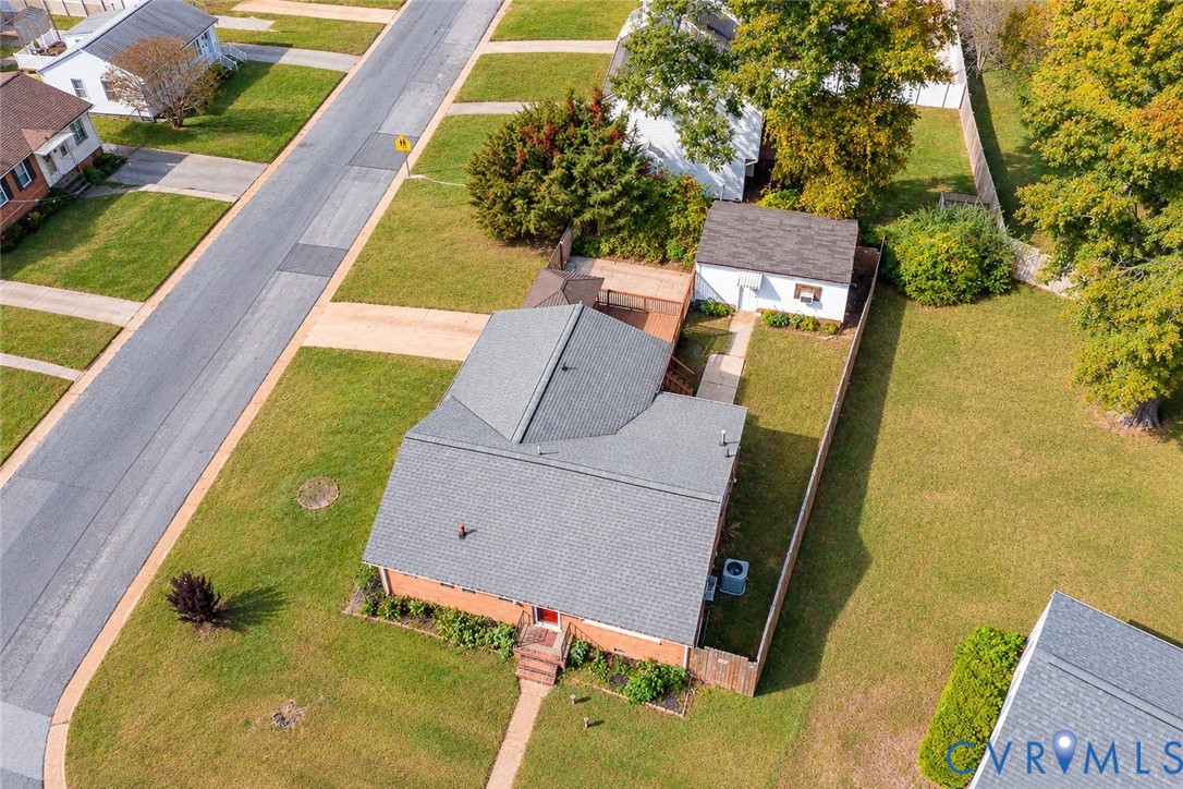 Aerial view of property featuring a brick exterior, shingled roof, detached garage, and fenced backyard with mature trees Aerial view of property featuring a brick exterior, shingled roof, detached garage, and fenced backyard with mature trees