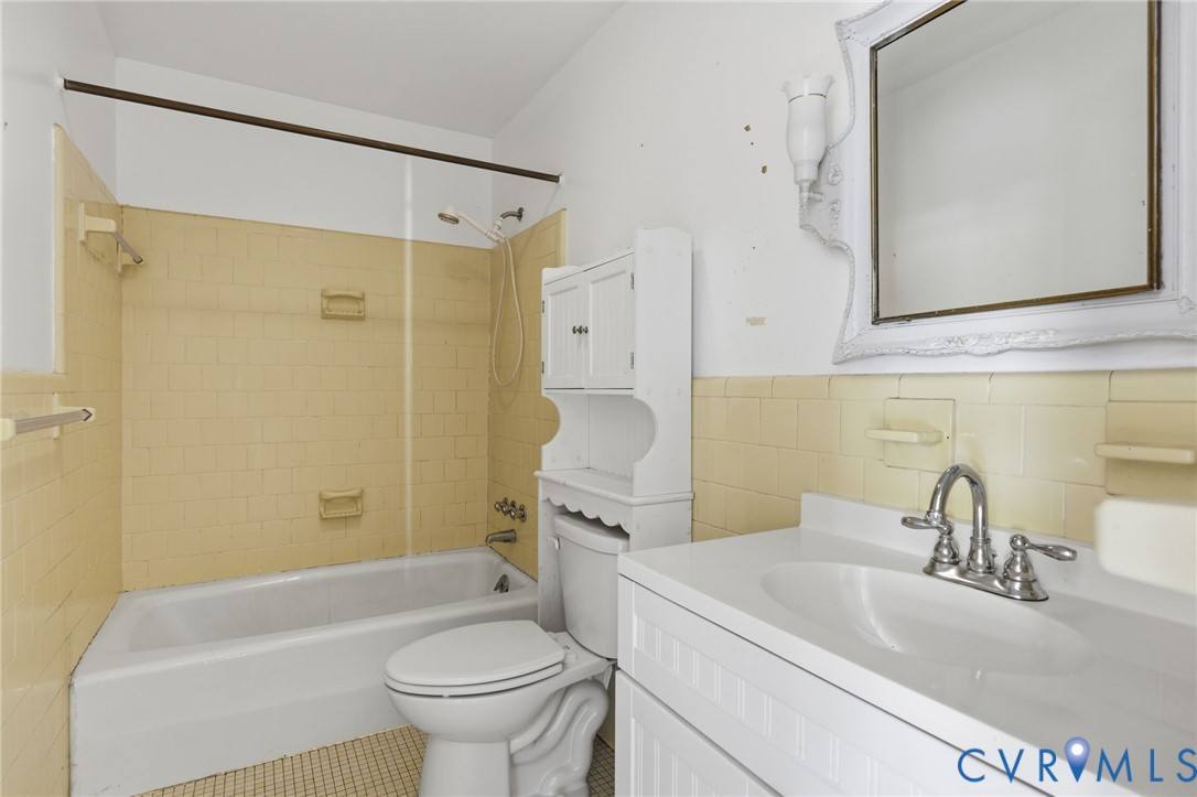 Bathroom featuring a porcelain tub and shower combination with tiled surround, integrated vanity with a basin sink, and wall-mounted mirror