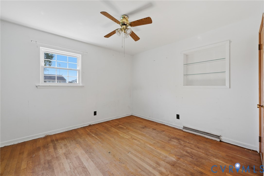 Wood-finish flooring, multi-pane window, built-in recessed shelving with glass inserts, and ceiling fan with integrated light fixture