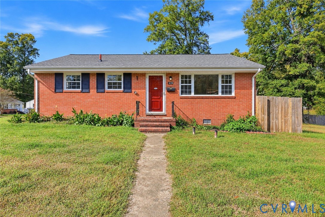 Single-story brick exterior featuring a shingled hip roof, dark shutter accents, a central red entry door, and a wooden privacy fence