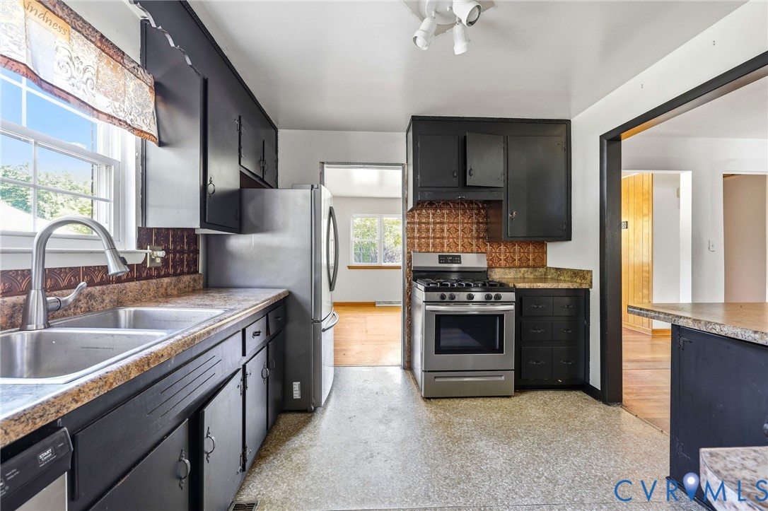 Kitchen featuring dark cabinetry, stainless steel appliances, decorative backsplash, and stone-finish countertops with an integrated dual-basin sink