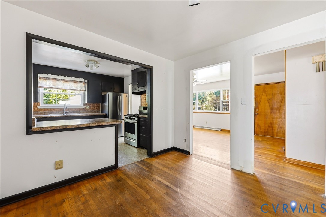 Kitchen featuring a passthrough window, stone-finish countertop, stainless steel refrigerator, stainless steel gas range, and wood-finish flooring