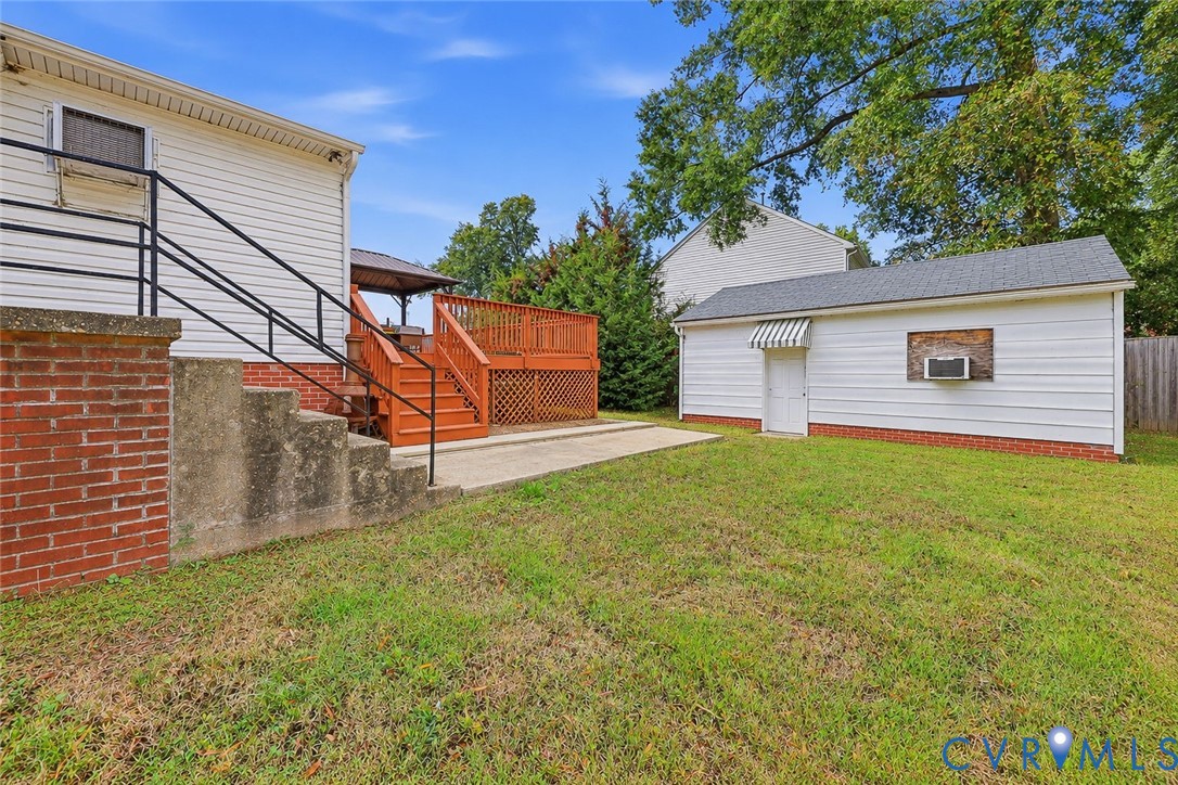 Rear exterior featuring a tiered wood deck, concrete patio, detached garage, and brick foundation accents
