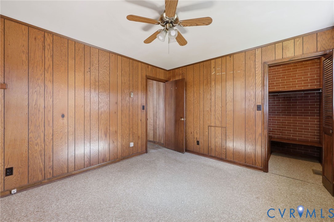 Vertical wood-paneled walls, ceiling fan with integrated lighting, and a closet featuring exposed brick interior masonry