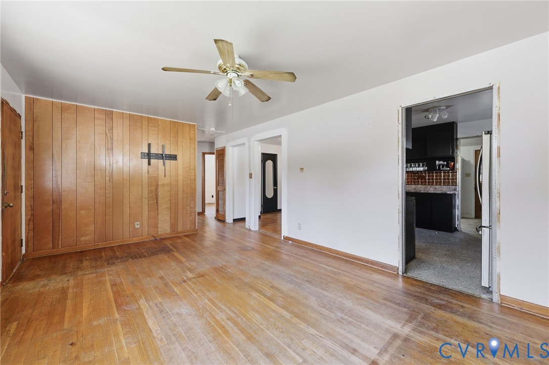 Interior space featuring wood-paneled accent wall, wood-finish flooring, and ceiling-mounted fan with integrated lighting