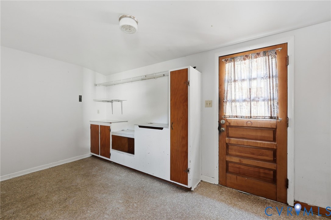 Built-in cabinetry with wood-finish paneling, overhead wire shelving, solid wood door with glass inset, and a ceiling-mounted light fixture