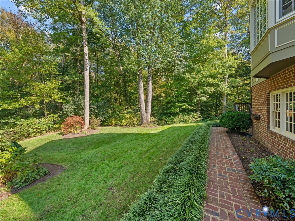 Brick exterior featuring a herringbone-patterned brick walkway, manicured lawn, and mature woodland canopy