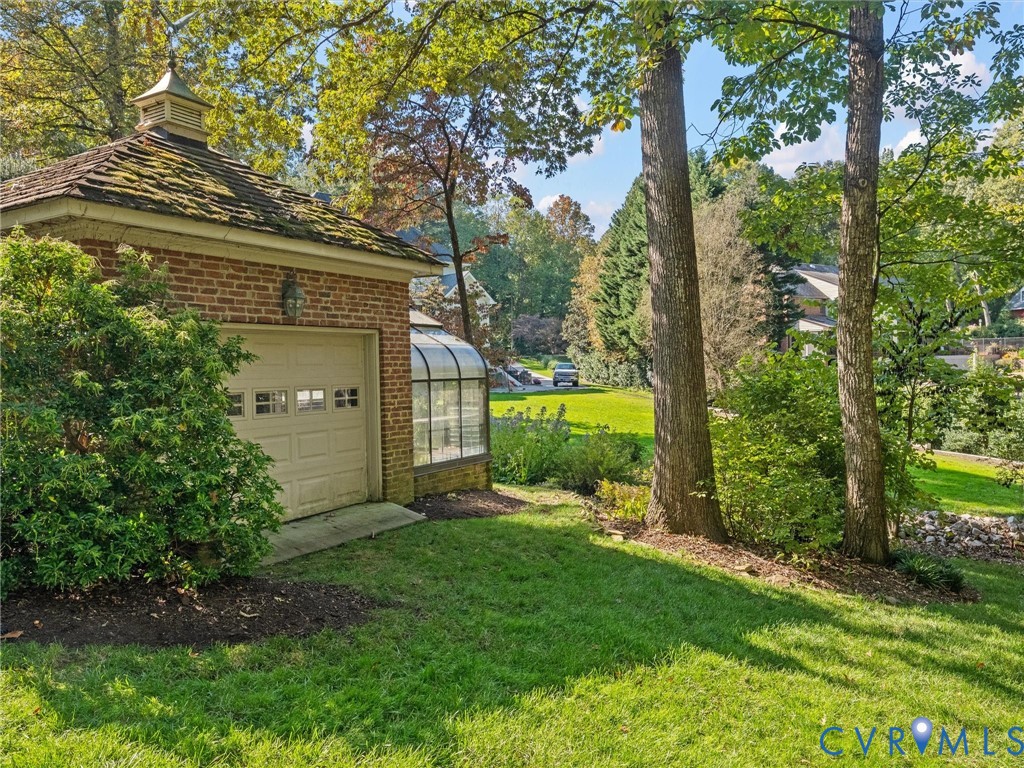 Brick exterior structure featuring a cupola, shingled roof, attached glass greenhouse, and segmented overhead door
