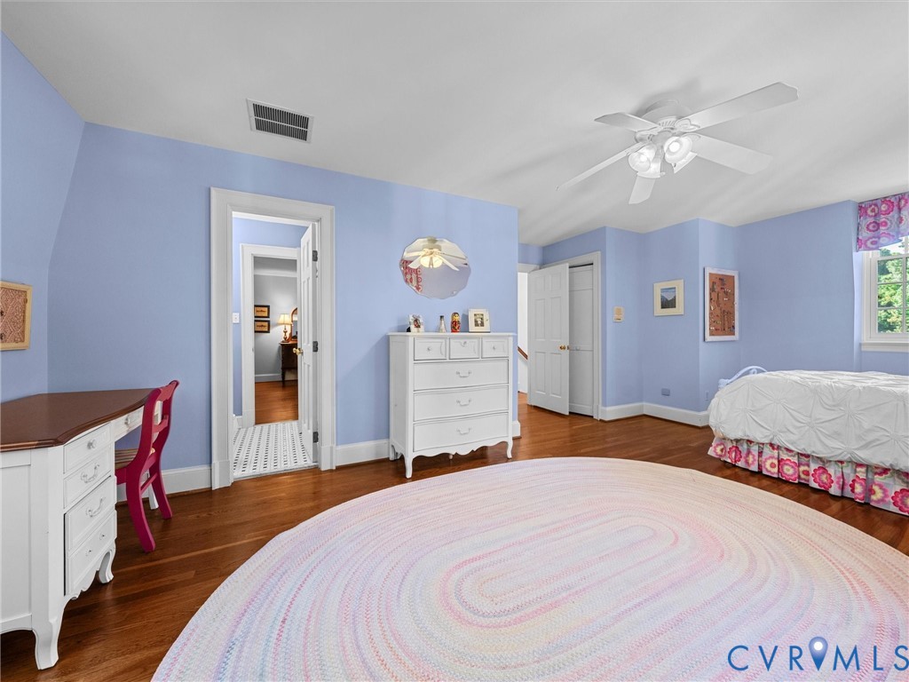 Bedroom featuring polished wood-finish flooring, a multi-blade ceiling fan with integrated light fixture, and two panel-door closets