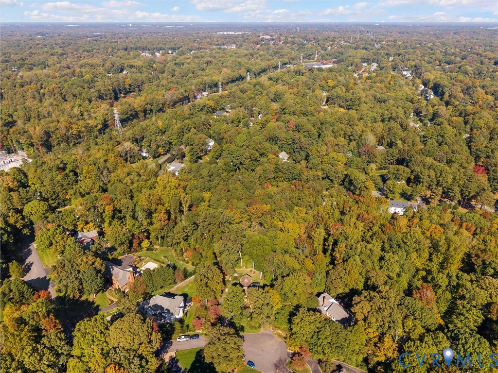 Aerial perspective featuring a sprawling wooded lot with established tree canopy and paved road access