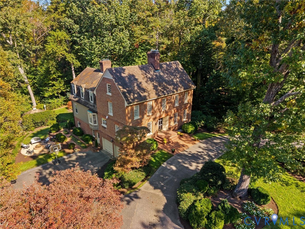 Colonial-style brick exterior featuring a multi-gabled roofline, dormer windows, a circular paved driveway, and an expansive wooded lot with mature trees
