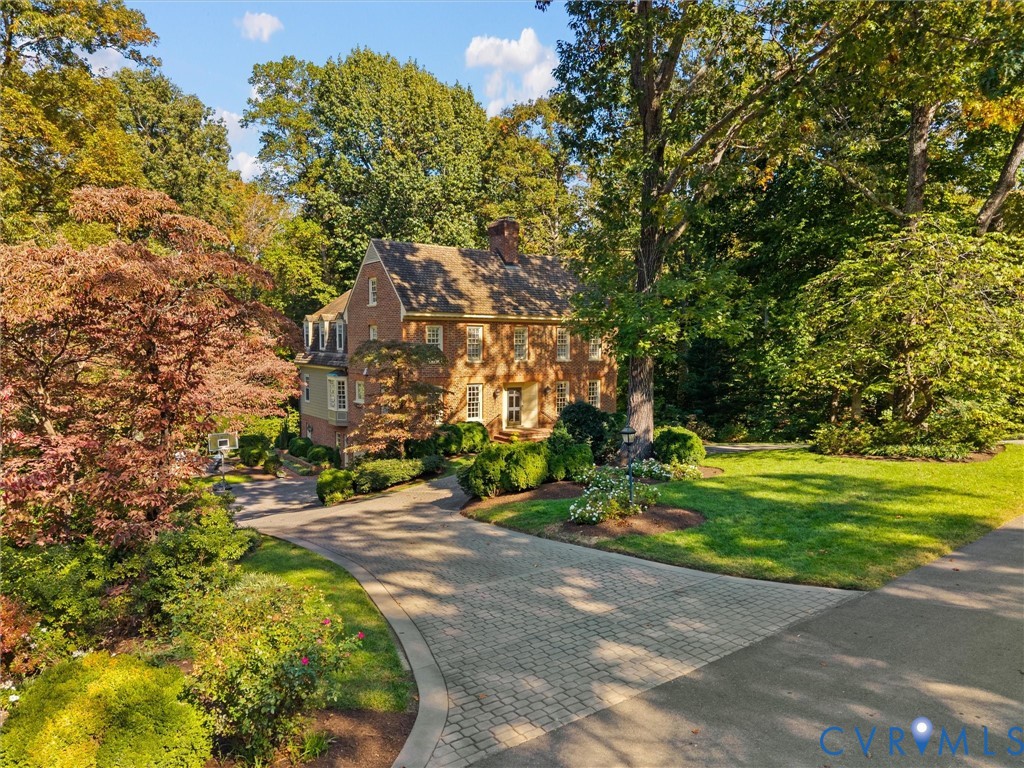 Brick exterior Colonial-style residence featuring a multi-gabled roofline, dormer windows, a paved stone driveway, and established landscaping