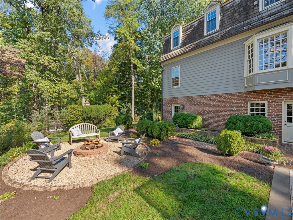 Brick and siding exterior featuring a multi-level roofline, circular fire pit area with stone edging, gravel patio surface, and landscaped garden beds