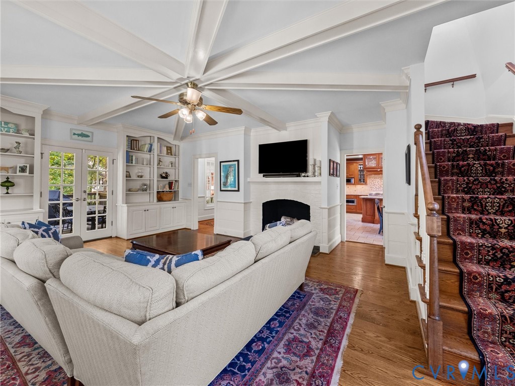 Vaulted ceiling with decorative beams, wood-finish flooring, built-in floor-to-ceiling cabinetry, and a masonry fireplace