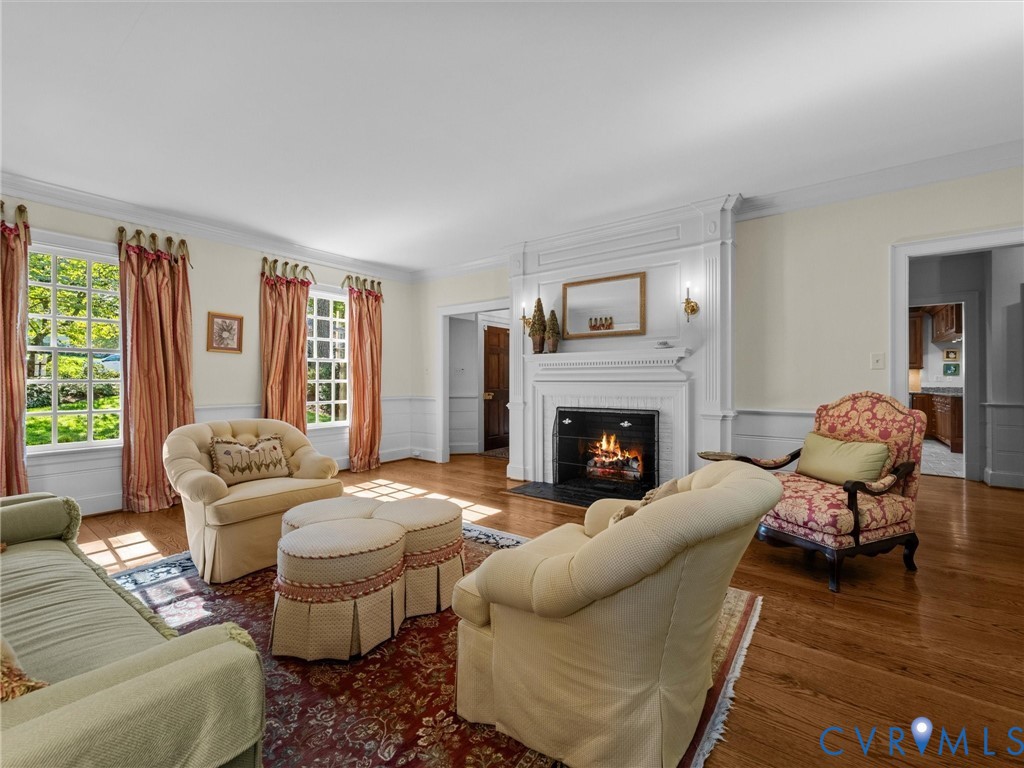 Living room featuring a classic fireplace with white wood mantel and paneling, hardwood flooring, multi-pane windows, and chair rail millwork