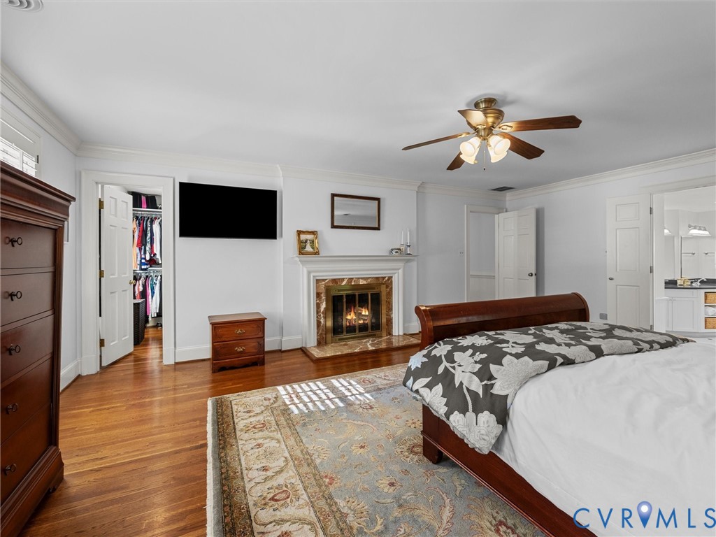 Fireplace with a stone surround and mantel, wood-finish flooring, ceiling fan with integrated lighting, and crown molding