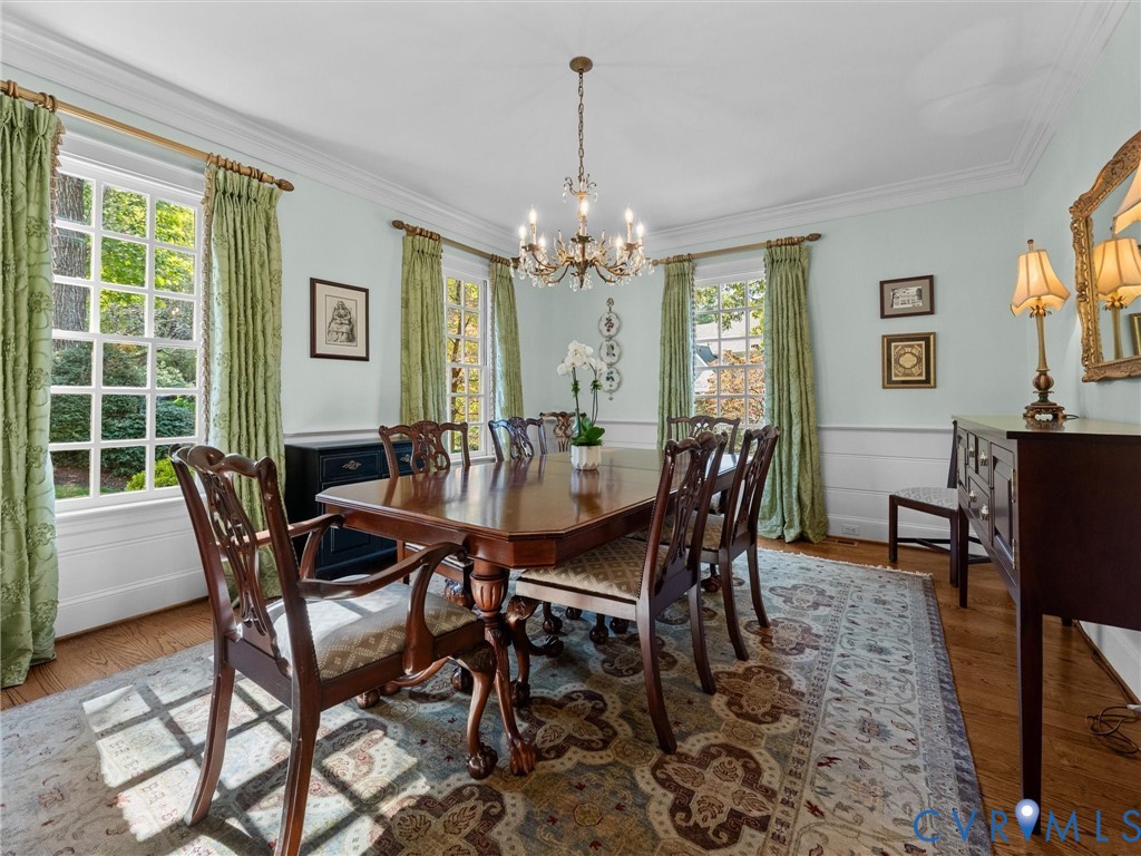 Formal dining space featuring multi-pane windows, crown molding, chair rail wainscoting, wood-finish flooring, and a central multi-arm chandelier