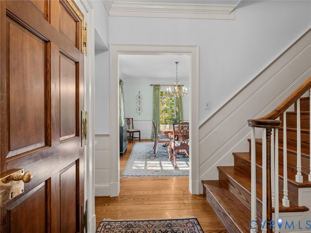 Foyer entrance featuring a solid wood door with brass hardware, wood-finish flooring, and a staircase with white balusters and a wood handrail