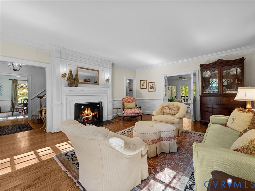 Living area featuring hardwood flooring, a fireplace with floor-to-ceiling millwork surround, crown molding, chair rail, and French doors