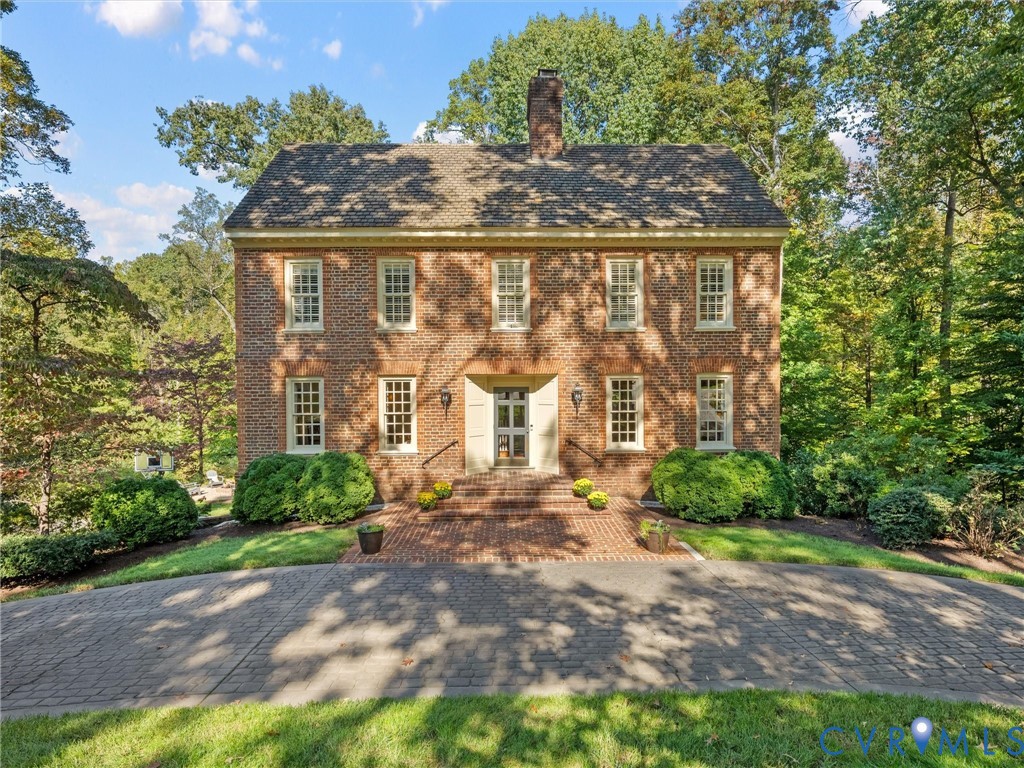 Traditional brick exterior featuring a central chimney, symmetrical multi-pane windows, a detailed cornice, and a brick-paved entry path