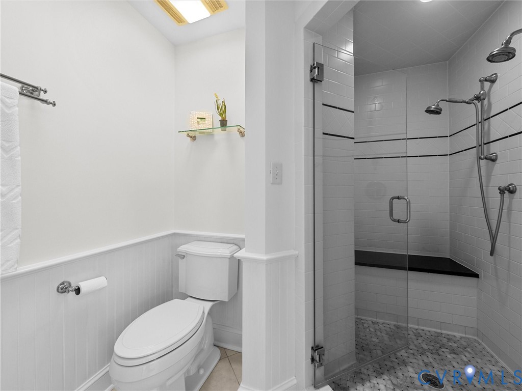 Walk-in shower with a glass door, built-in stone bench, and multi-setting shower head