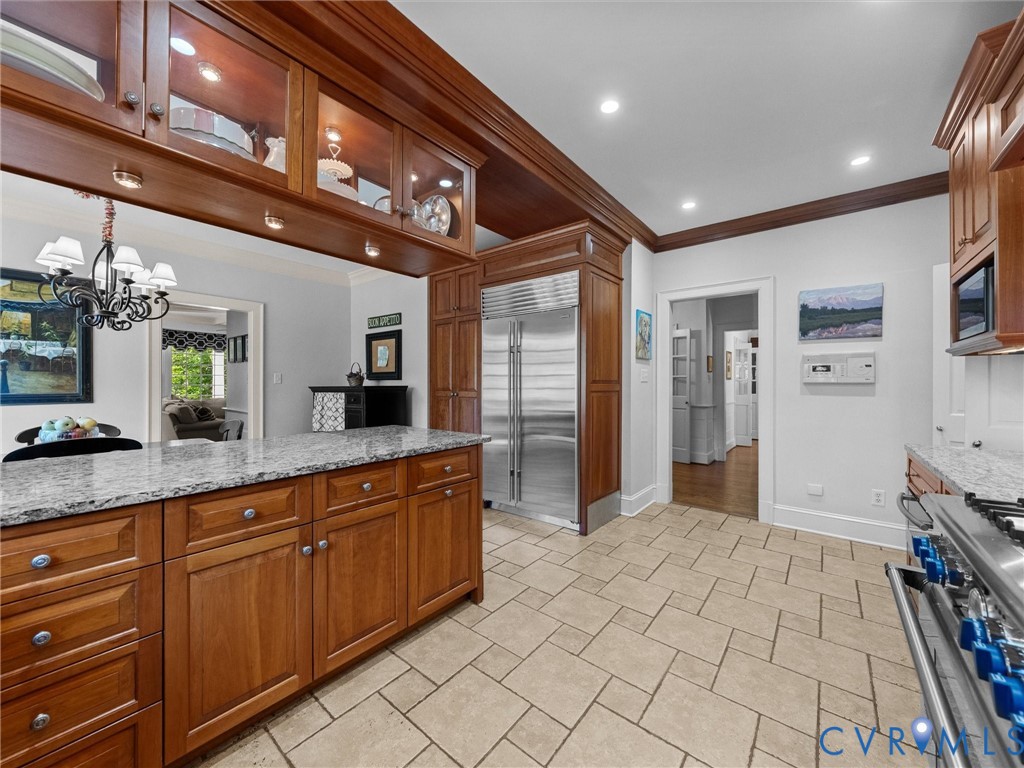 Kitchen featuring custom wood cabinetry, granite countertops, professional-grade stainless steel refrigerator, stone tile flooring, and integrated display cabinets