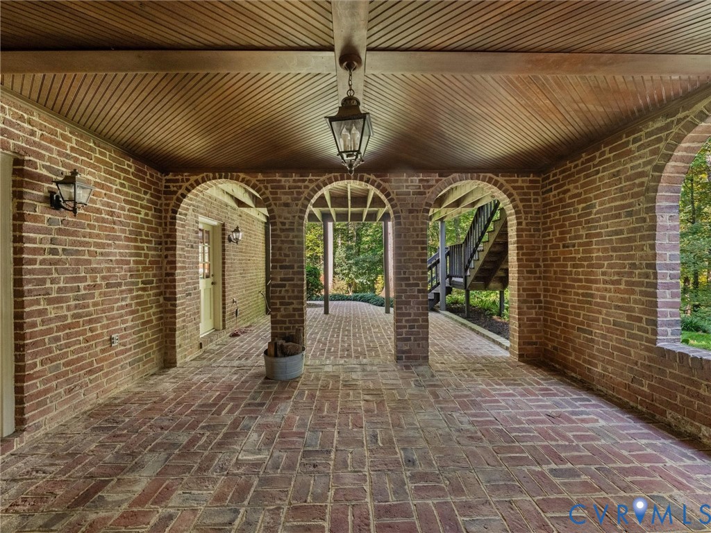 Covered patio featuring intricate brick archways, a herringbone brick floor, beadboard ceiling, and wall-mounted carriage-style lighting