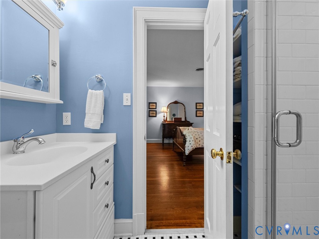 Bathroom featuring a white vanity cabinet with a solid surface countertop, chrome faucet, medicine cabinet, and a glass-enclosed shower with white subway tile surround