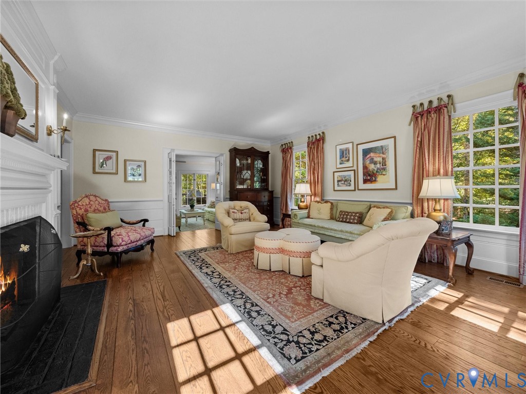 Living room featuring wood-finish flooring, crown molding, chair rail trim, and a fireplace with a decorative mantel