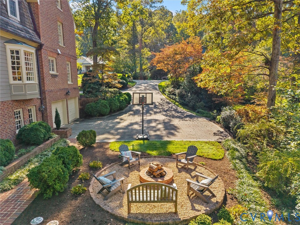 Brick exterior featuring a circular gravel fire pit, paved driveway, mature trees, and landscaped shrubbery