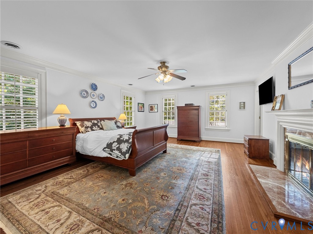 Spacious room featuring wood flooring, crown molding, multi-pane windows, and a fireplace with a stone-surround hearth