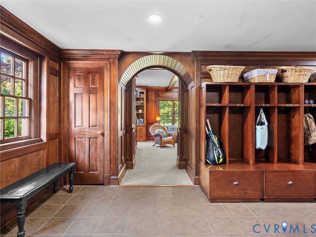 Custom wood-paneled walls, built-in wooden storage cubbies, arched architectural detail, multi-pane window, and tile flooring