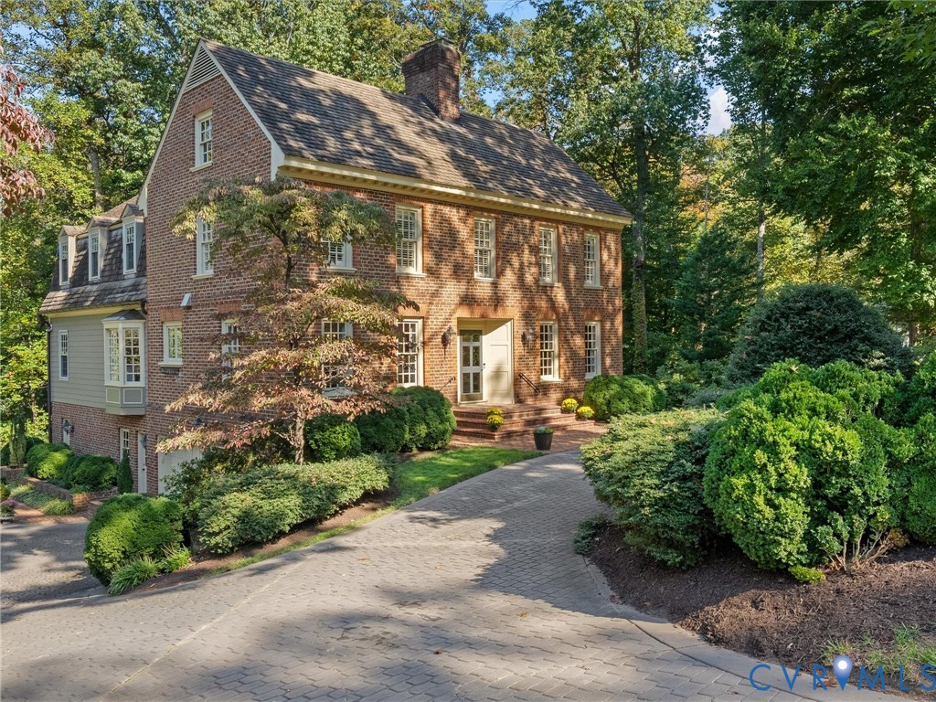 Classic brick exterior with a gable roof, decorative dentil molding, bay window, and a paved stone driveway