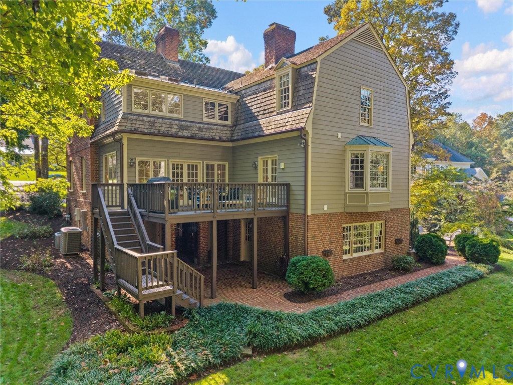 Multi-story Dutch Colonial exterior featuring a combination of brick and horizontal siding, a raised wooden deck, a lower-level brick patio, and a bay window