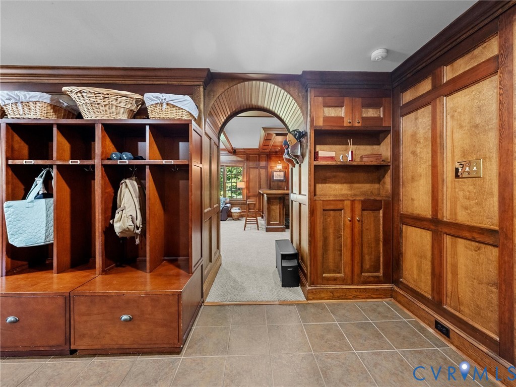 Custom wood-paneled wall cabinetry featuring integrated shelving, built-in storage lockers, and lower pull-out drawers, complemented by an arched architectural entryway and ceramic tile flooring