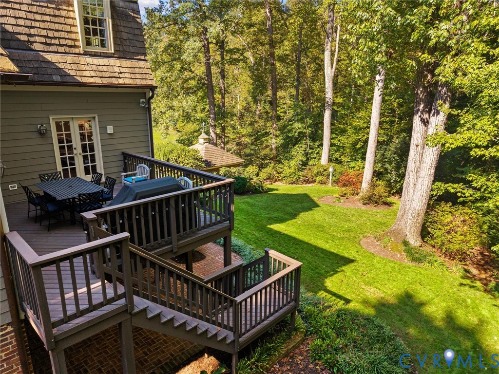 Multi-level wood deck with balustrades, brick patio, and expansive lawn featuring mature trees