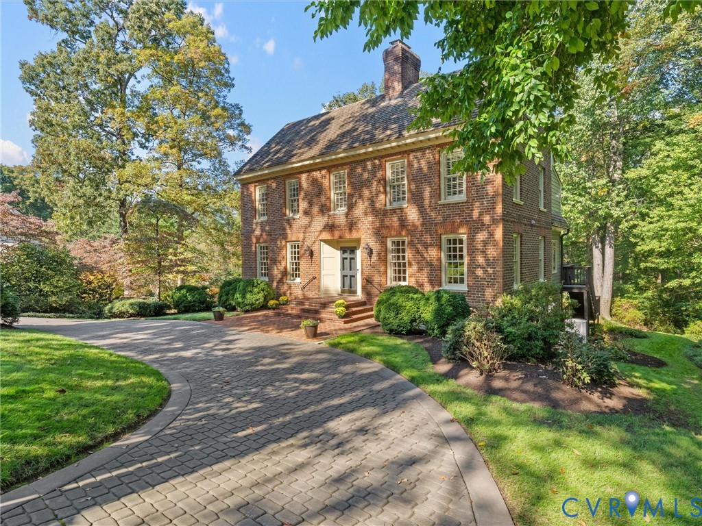 Two-story brick exterior featuring a multi-pane window configuration, a central chimney, and a paved circular driveway leading to a brick-accented entryway