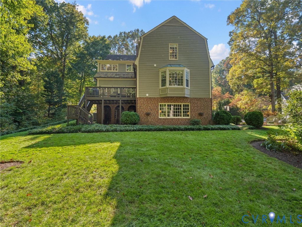 Multi-level exterior featuring a brick and horizontal siding facade, a raised wooden deck with stairs, a multi-pane bay window, and a spacious lawn
